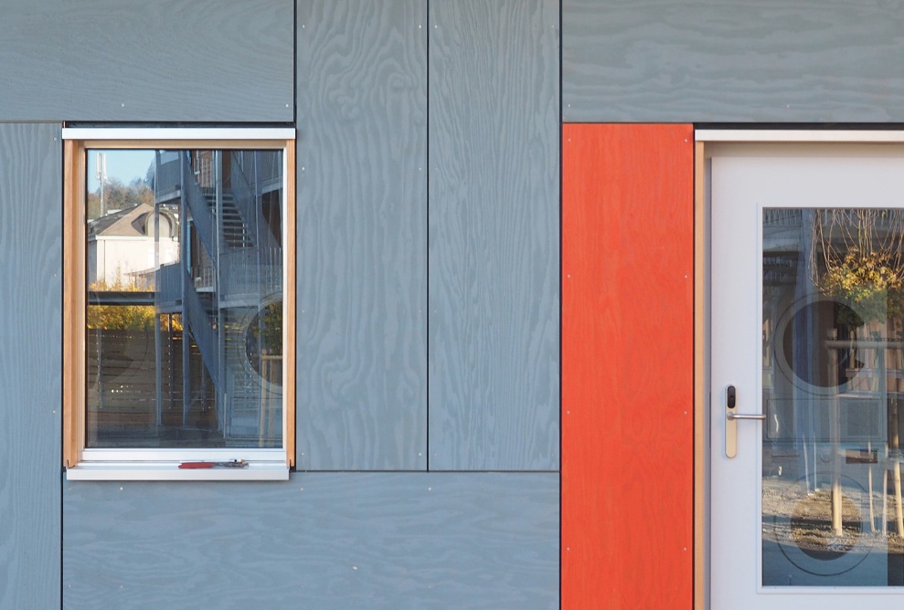 Prise de vue de la façade grise et rouge du centre d’accueil pour demandeurs d’asile Grosshof avec gros plan d’une fenêtre et d’une porte