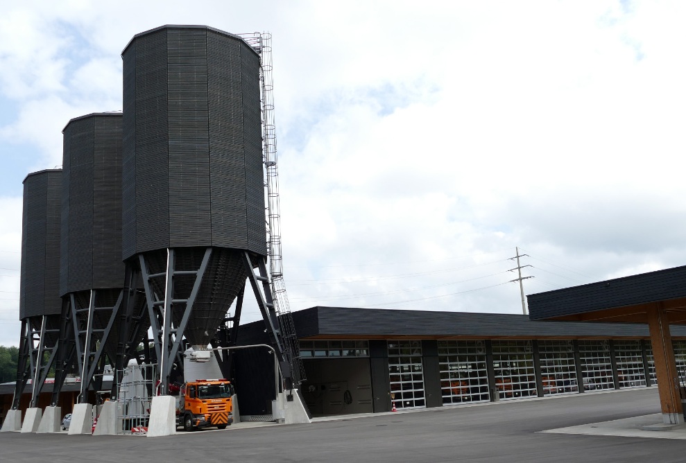 Trois silos dodécagonaux (E12) en bois de 900 m³ placés à côté d’un bâtiment d’atelier moderne avec la même façade noire